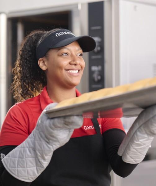 Smiling employee taking buns out of oven